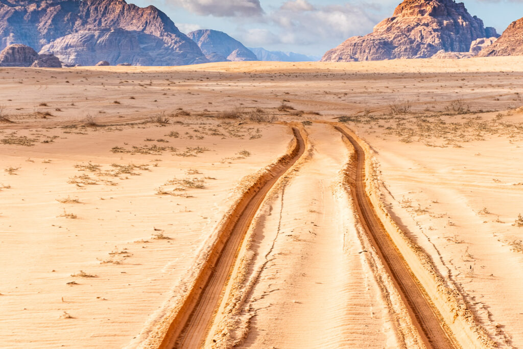 Marcas de pneus em curva na areia do deserto, com montanhas ao fundo.