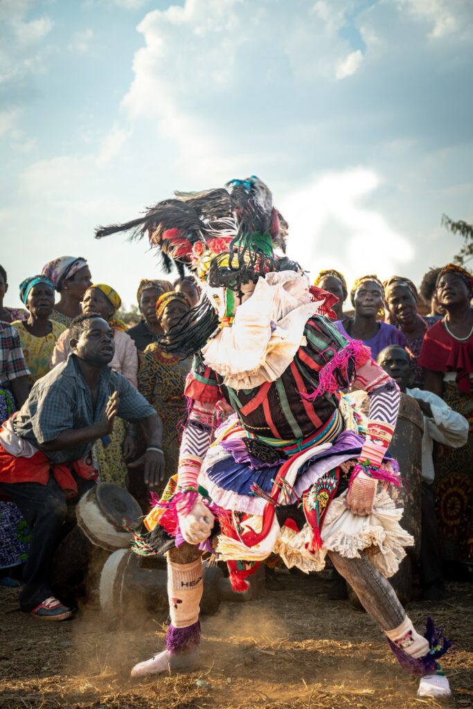 Dançarino Gule Wamkulu, com traje de tiras coloridas e máscara, dança em círculo diante da comunidade Chewa, no Malauí